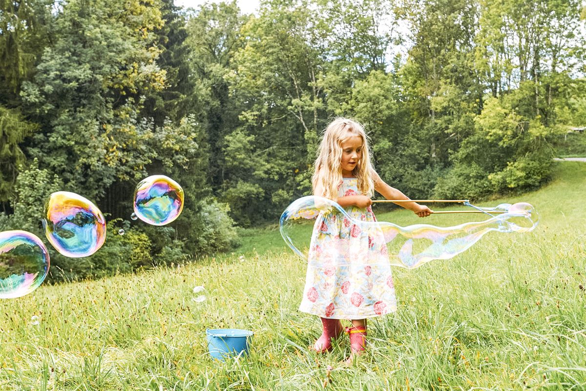Mädchen im Blumenkleid lässt Seifenblasen auf einer Wiese steigen