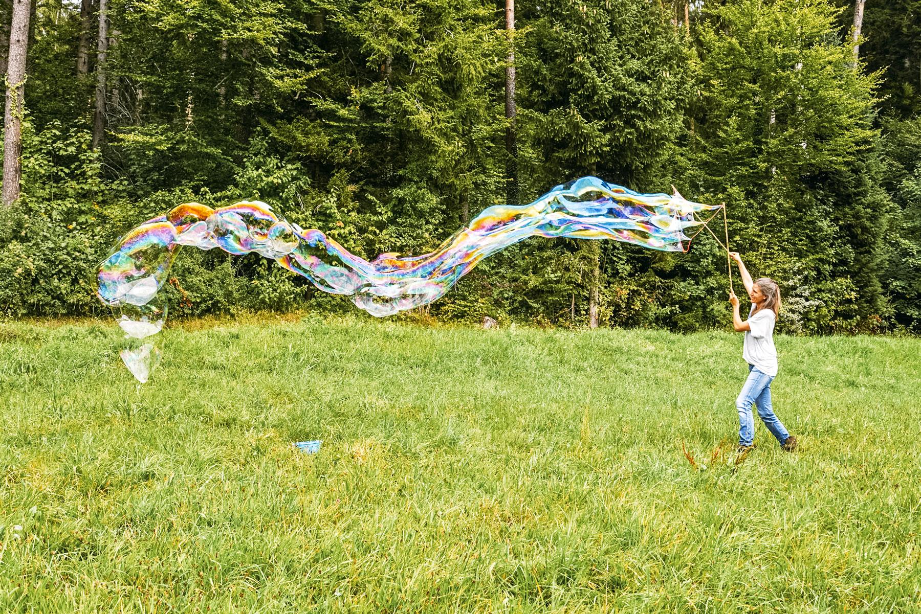Frau lässt in einer Wiese eine riesige, regenbogenbunte Seifenblase steigen